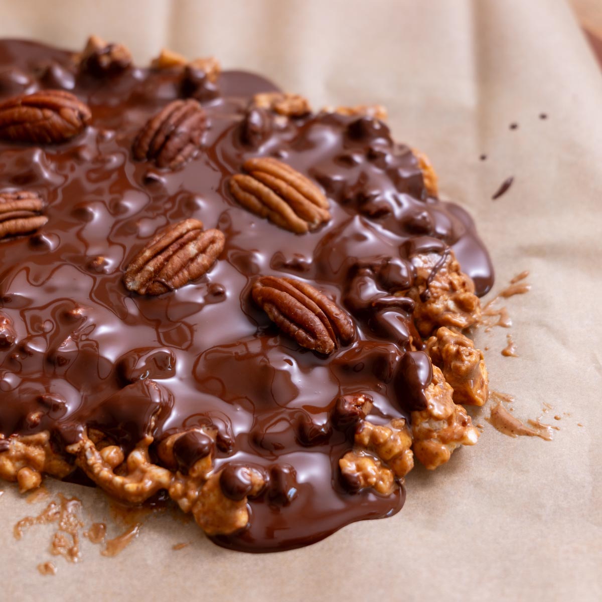 Close-up of crispy apple chocolate bark with melted dark chocolate and pecans on parchment paper