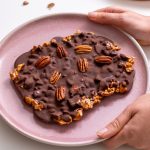 Sarah Cobacho holding a pink plate of crispy apple chocolate bark with pecans on top