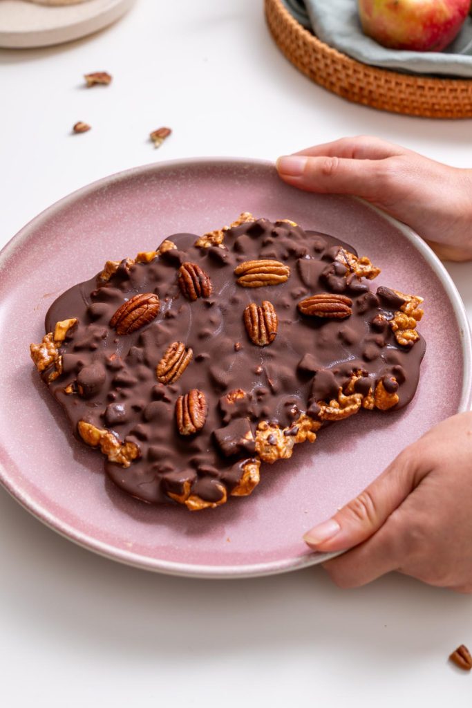 Sarah Cobacho holding a pink plate of crispy apple chocolate bark with pecans on top