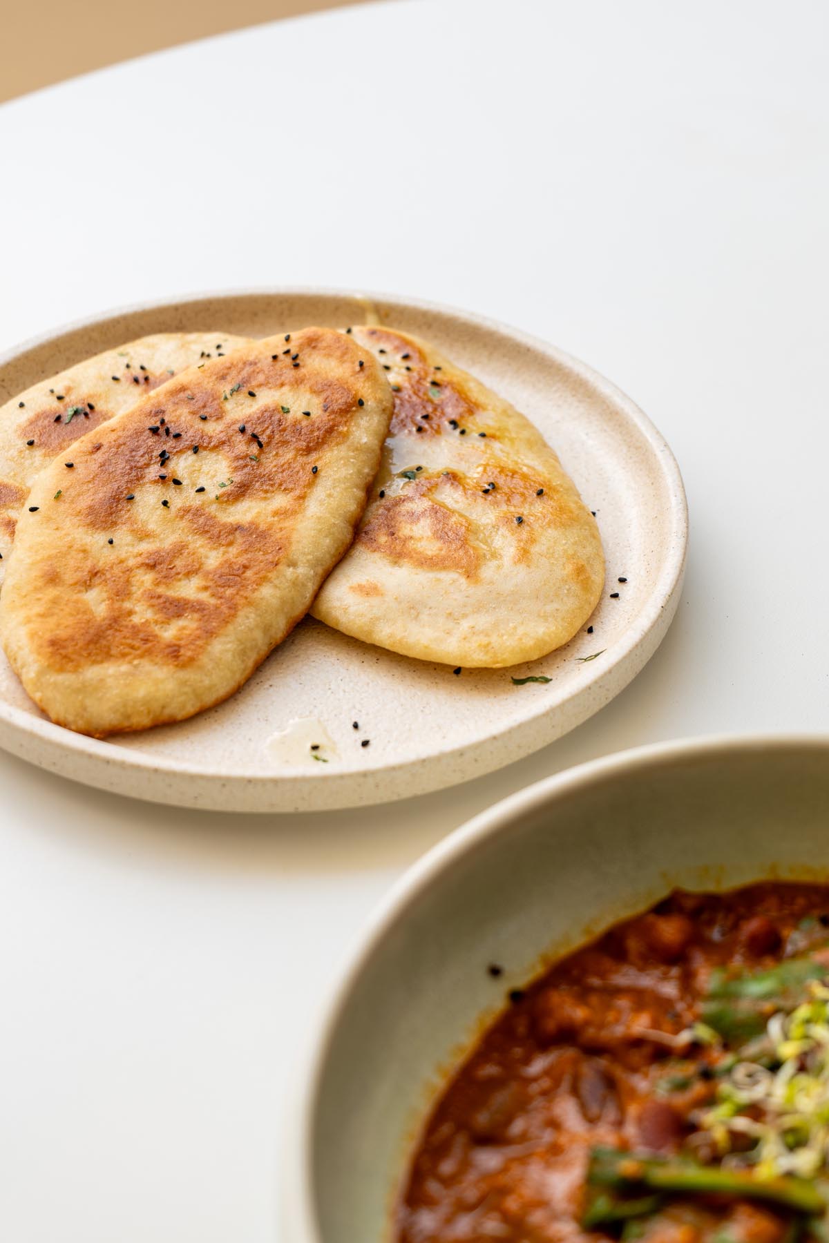 Two pieces of dairy-free naan bread on a plate next to a bowl of curry