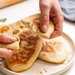 Sarah Cobacho holding and tearing a piece of dairy-free naan bread over a plate