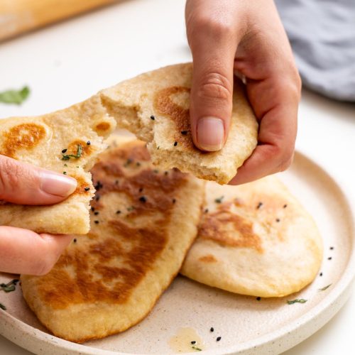 Sarah Cobacho holding and tearing a piece of dairy-free naan bread over a plate