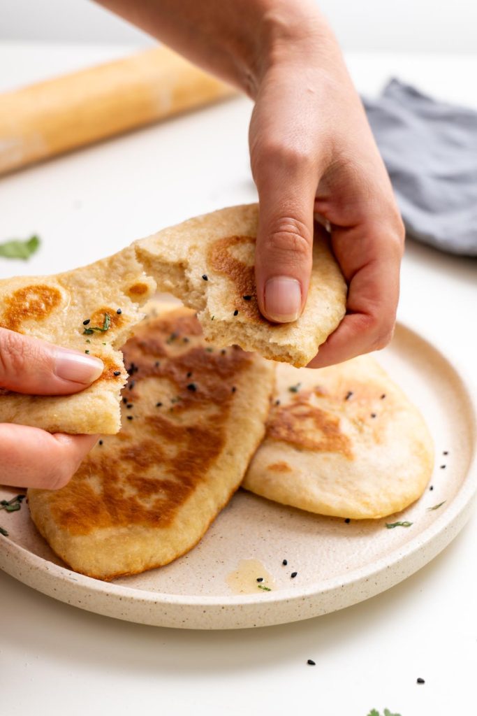 Sarah Cobacho holding and tearing a piece of dairy-free naan bread over a plate