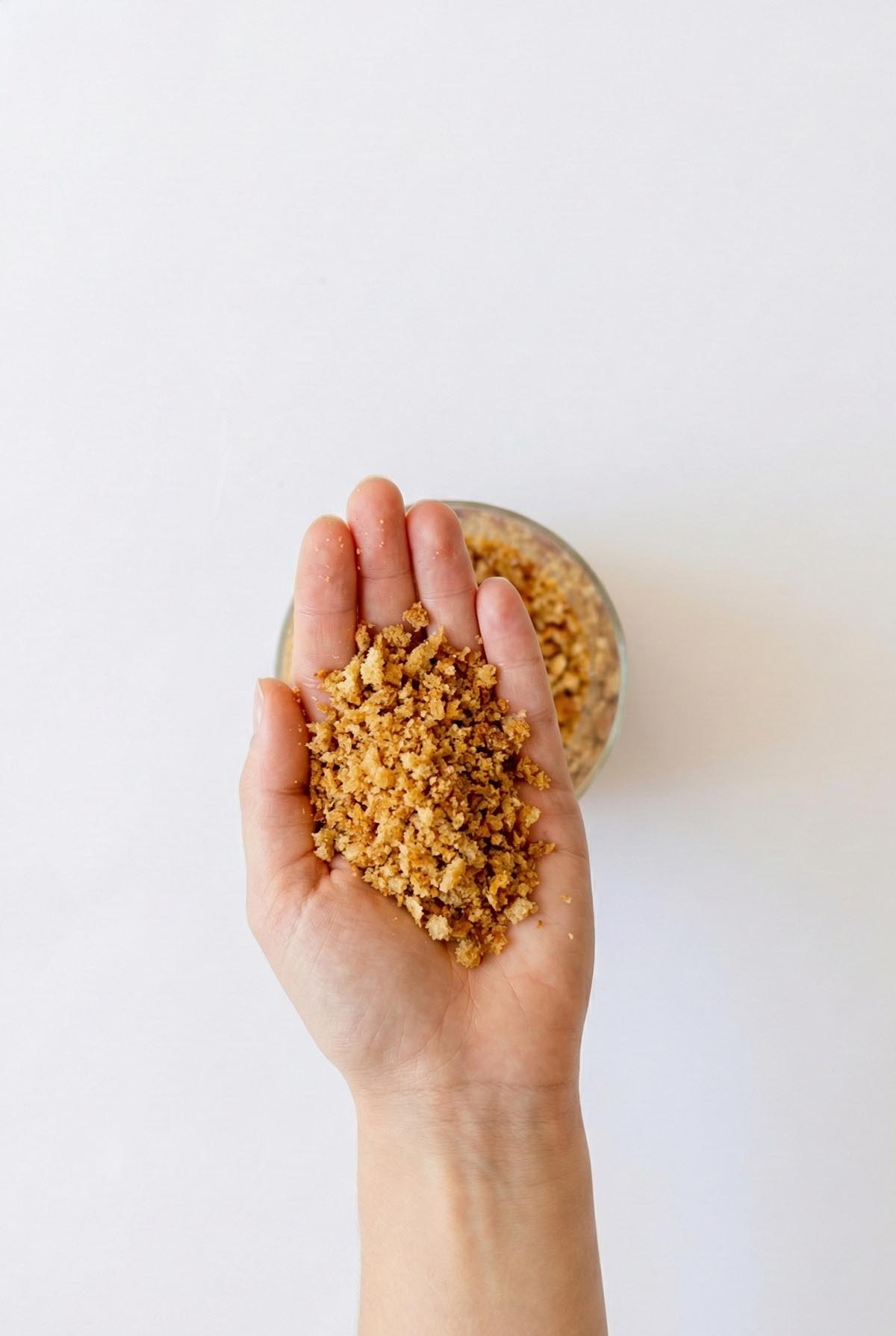 Sarah Cobacho holding a handful of golden homemade sourdough breadcrumbs over a clean white background