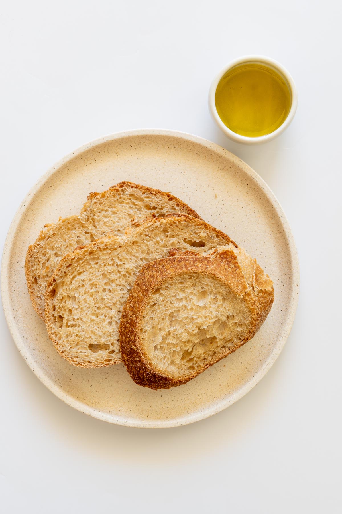 Slices of sourdough bread and a small dish of olive oil arranged on a neutral plate