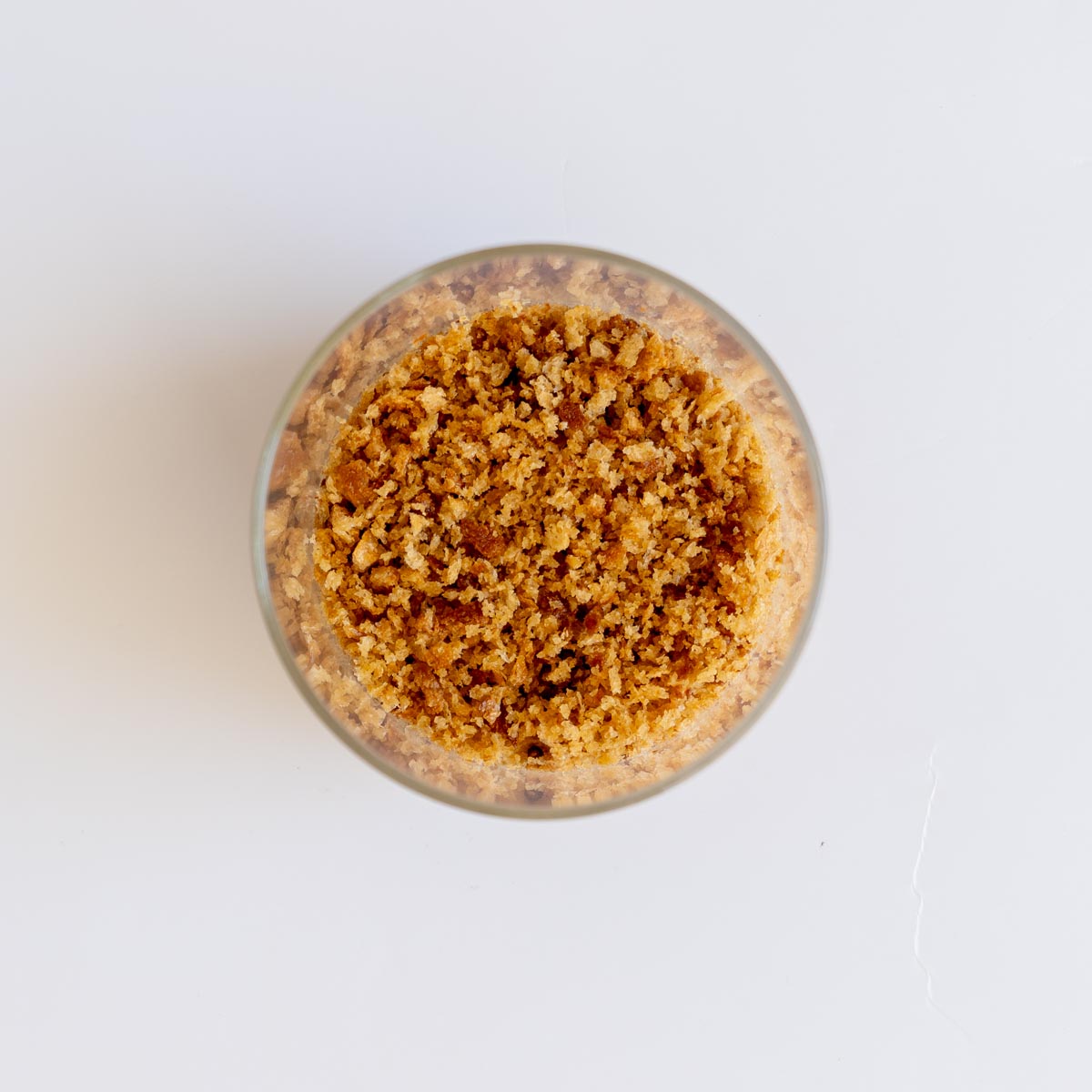 A glass jar filled with golden toasted homemade sourdough breadcrumbs on a white surface