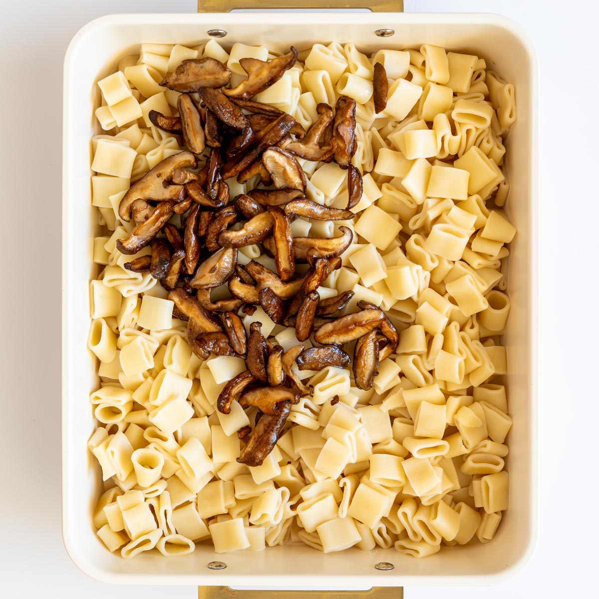 Cooked pasta in a baking dish topped with sautéed shiitake mushrooms.