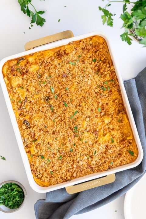 Baked mac and cheese in a white baking dish with crispy topping and fresh herbs