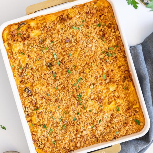 Baked mac and cheese in a white baking dish with crispy topping and fresh herbs
