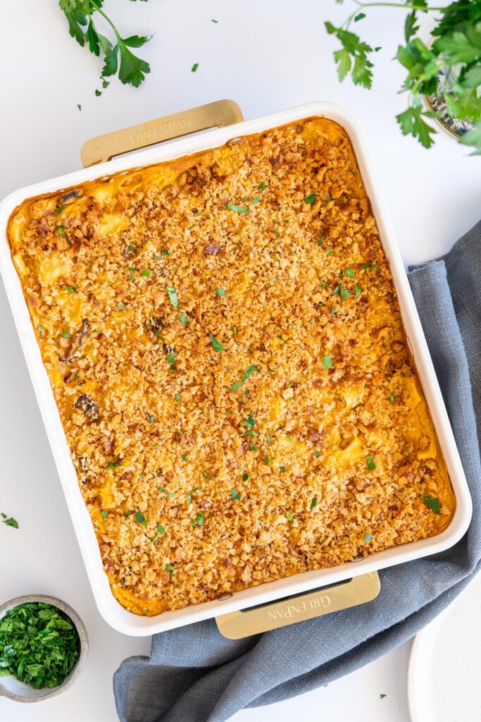 Baked mac and cheese in a white baking dish with crispy topping and fresh herbs