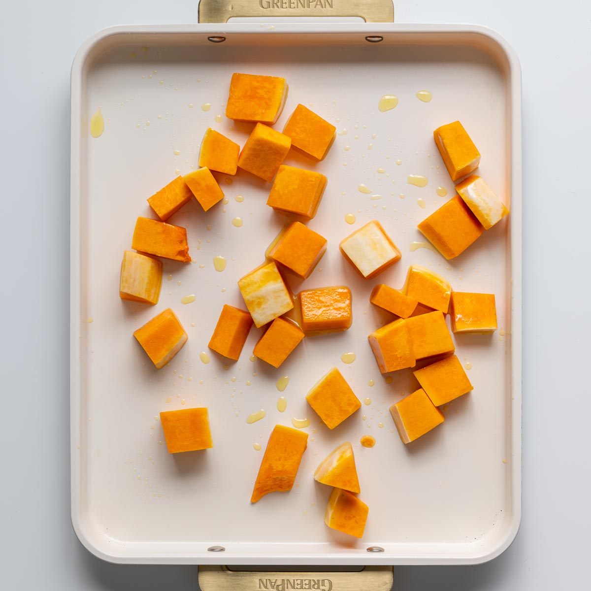 Pumpkin cubes arranged on a baking tray with a drizzle of olive oil before roasting