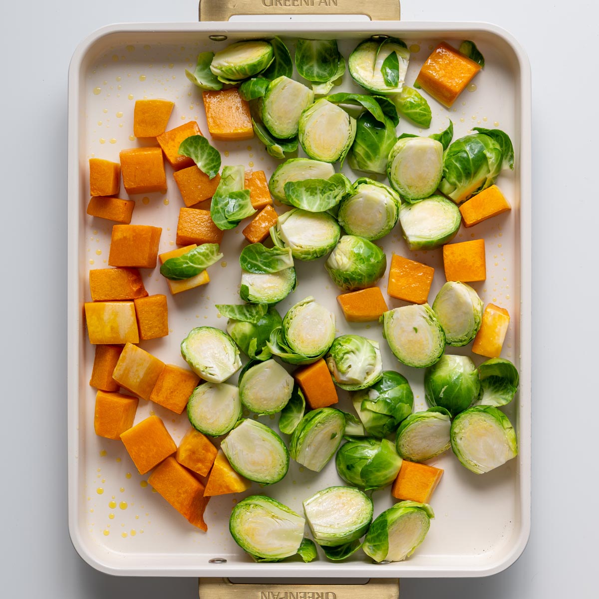 Pumpkin cubes and halved Brussels sprouts arranged on a baking tray before roasting
