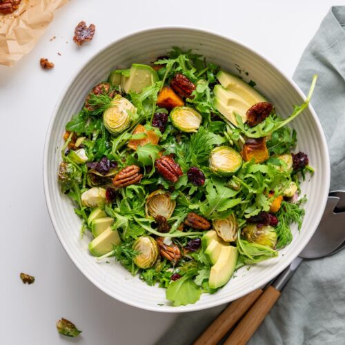 Holiday salad with greens, roasted vegetables, avocado, cranberries, pecans, and dill in a serving bowl