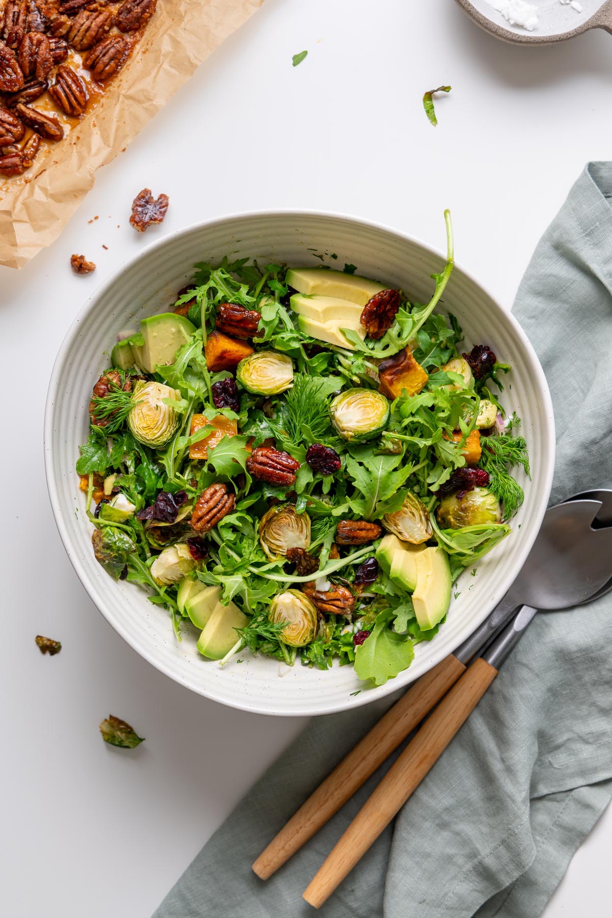 Overhead view of holiday salad with roasted vegetables, arugula, avocado, dill, and candied pecans ready to serve