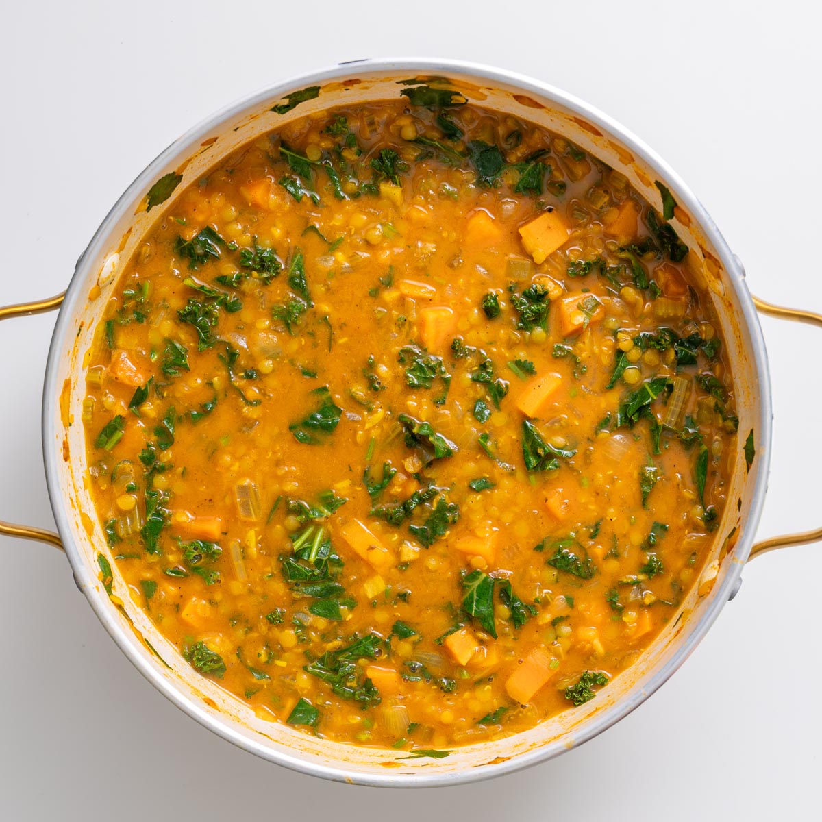 Creamy red lentil and sweet potato soup in a pot with kale stirred in.