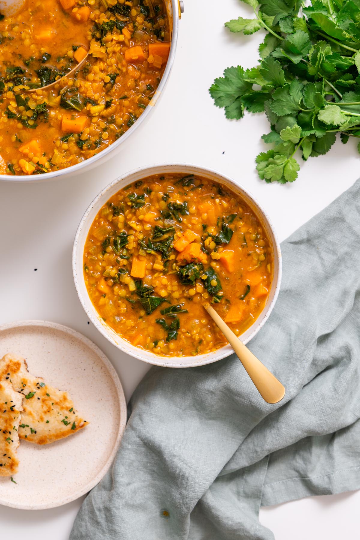 Bowl of creamy red lentil and sweet potato soup with kale, served with flatbread.