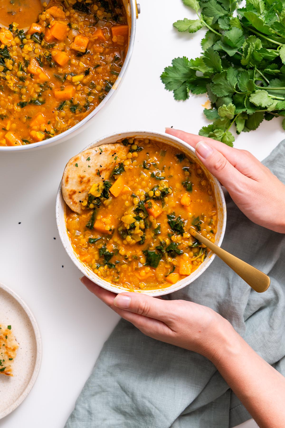 Sarah Cobacho holding a bowl of creamy red lentil and sweet potato soup with kale and naan.