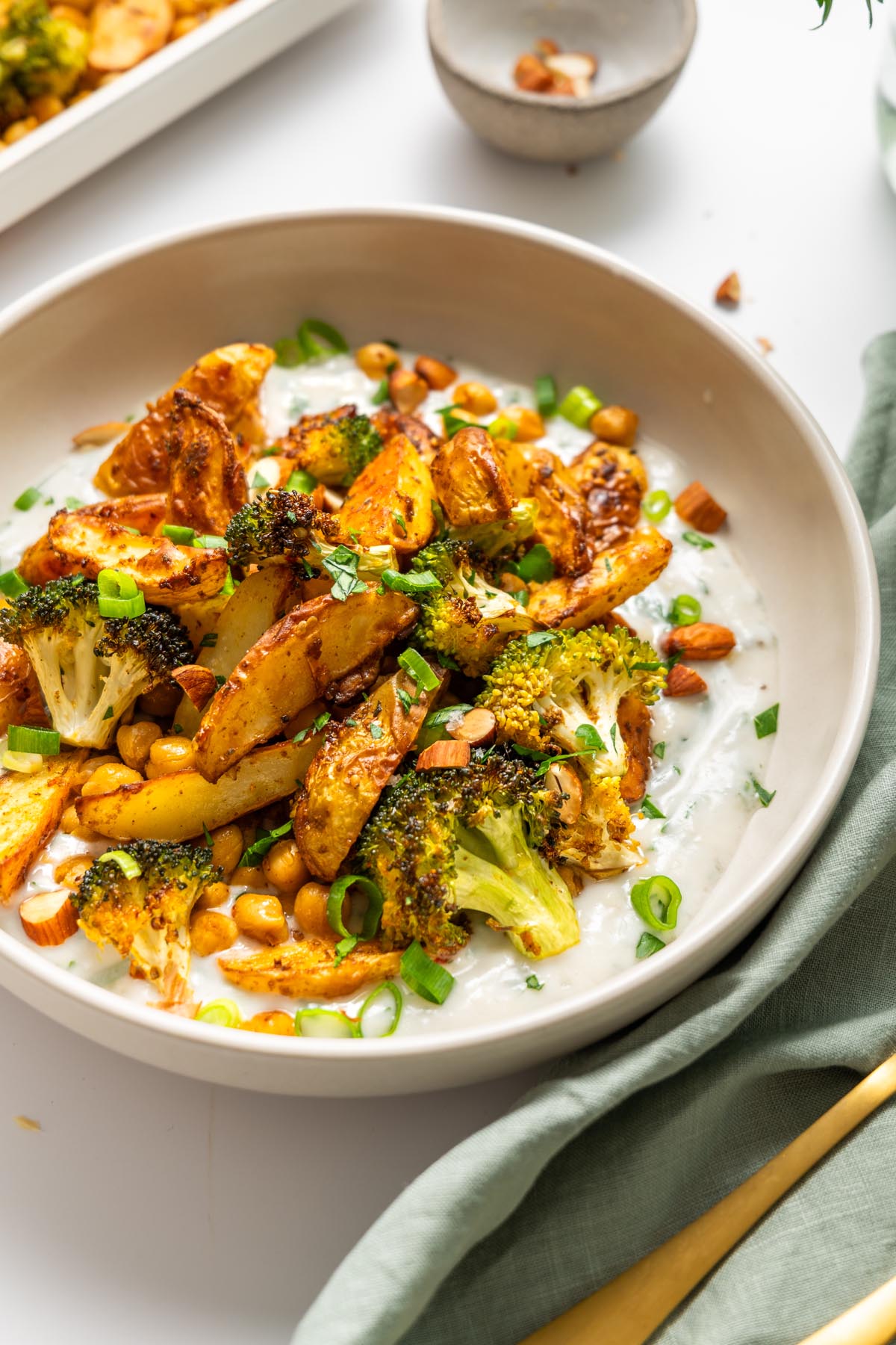 Close-up of roasted potatoes, broccoli, and chickpeas served on garlic yogurt sauce.