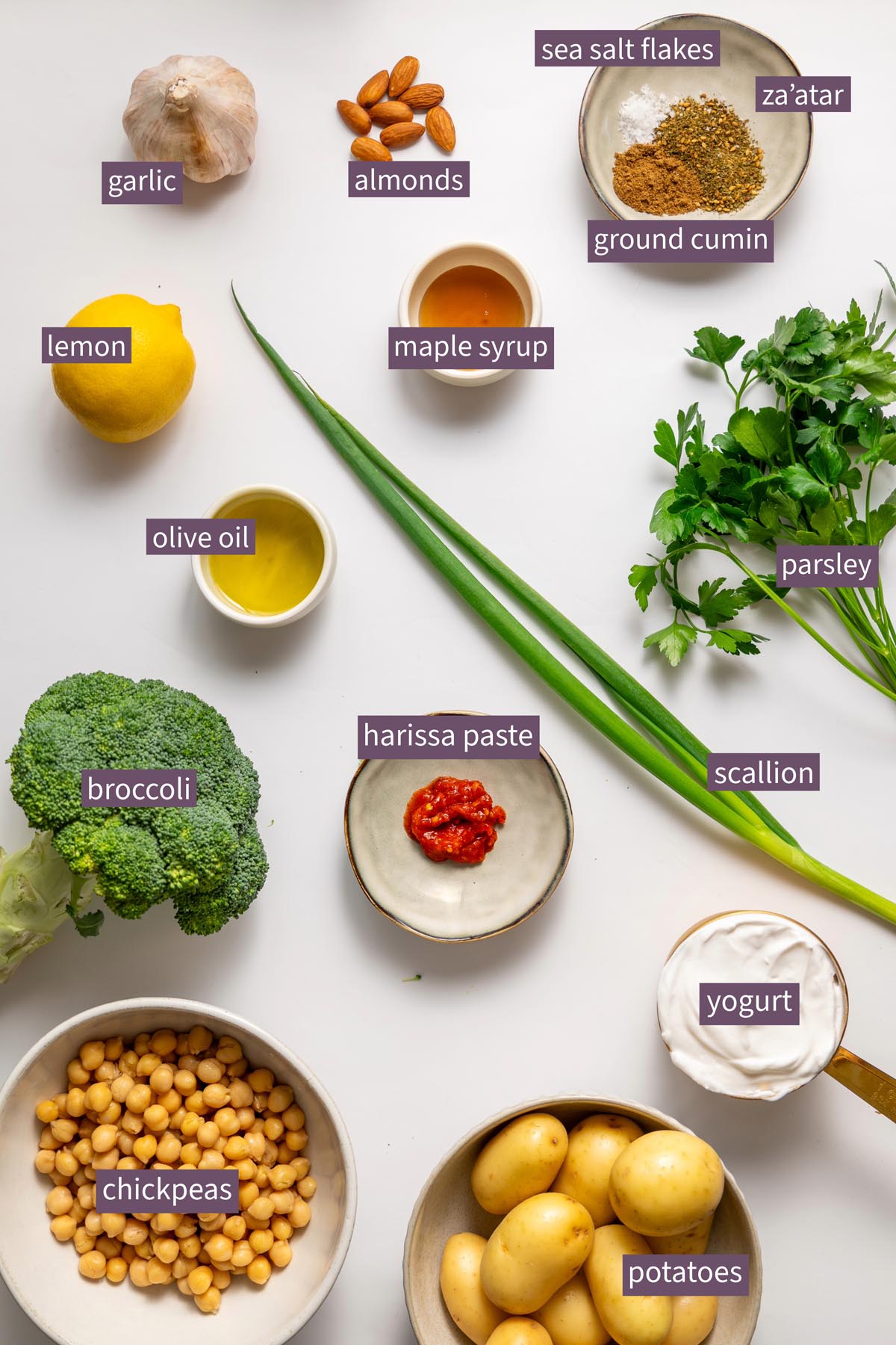 Colorful ingredients for roasted potato bowl with chickpeas, potatoes, broccoli, and spices on a white surface.