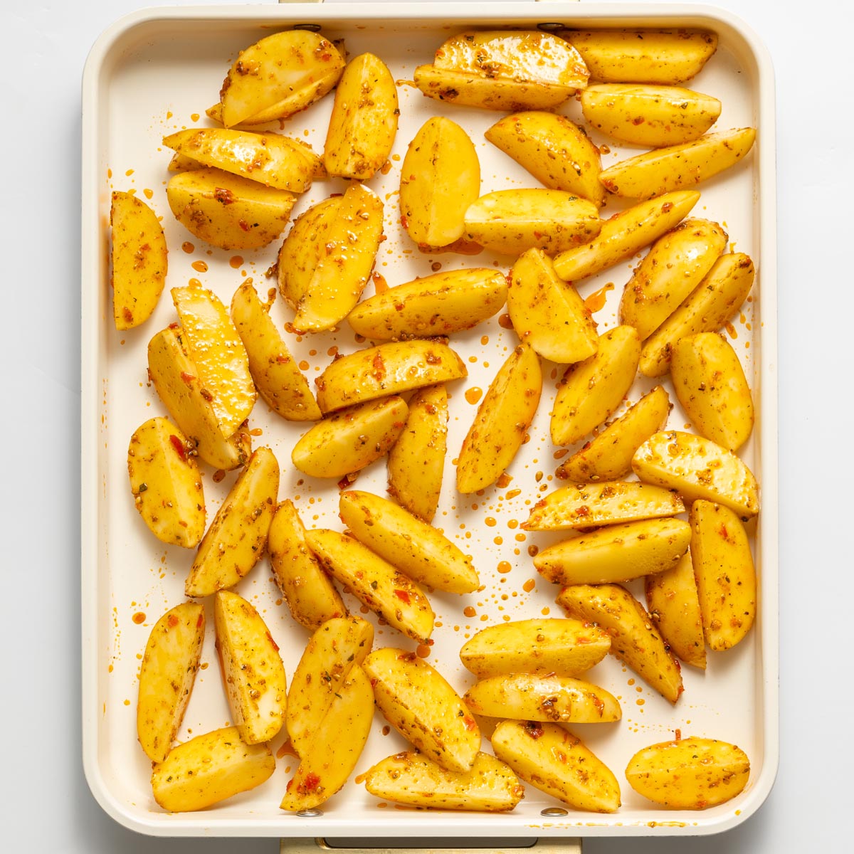Seasoned potato wedges coated in harissa and za’atar on a baking tray before roasting.