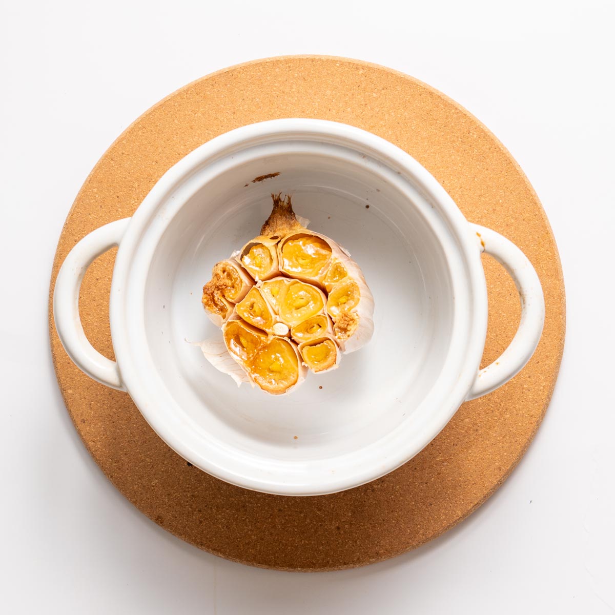 Golden roasted garlic confit in a small white baking dish.