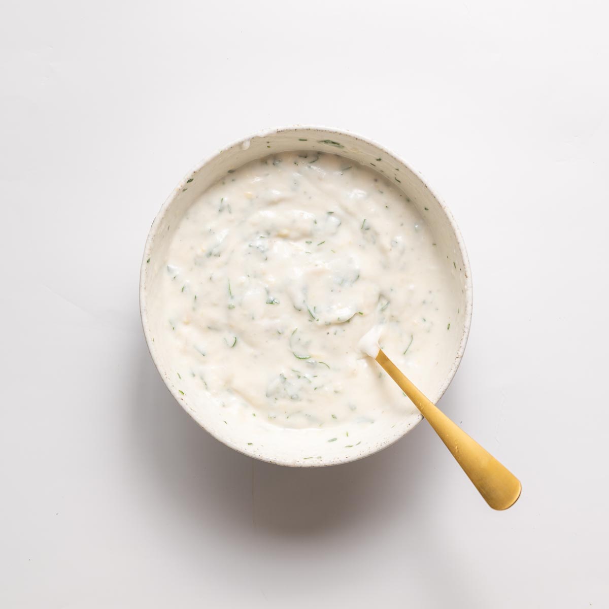 Creamy garlic yogurt sauce mixed with parsley in a white bowl with a gold spoon.