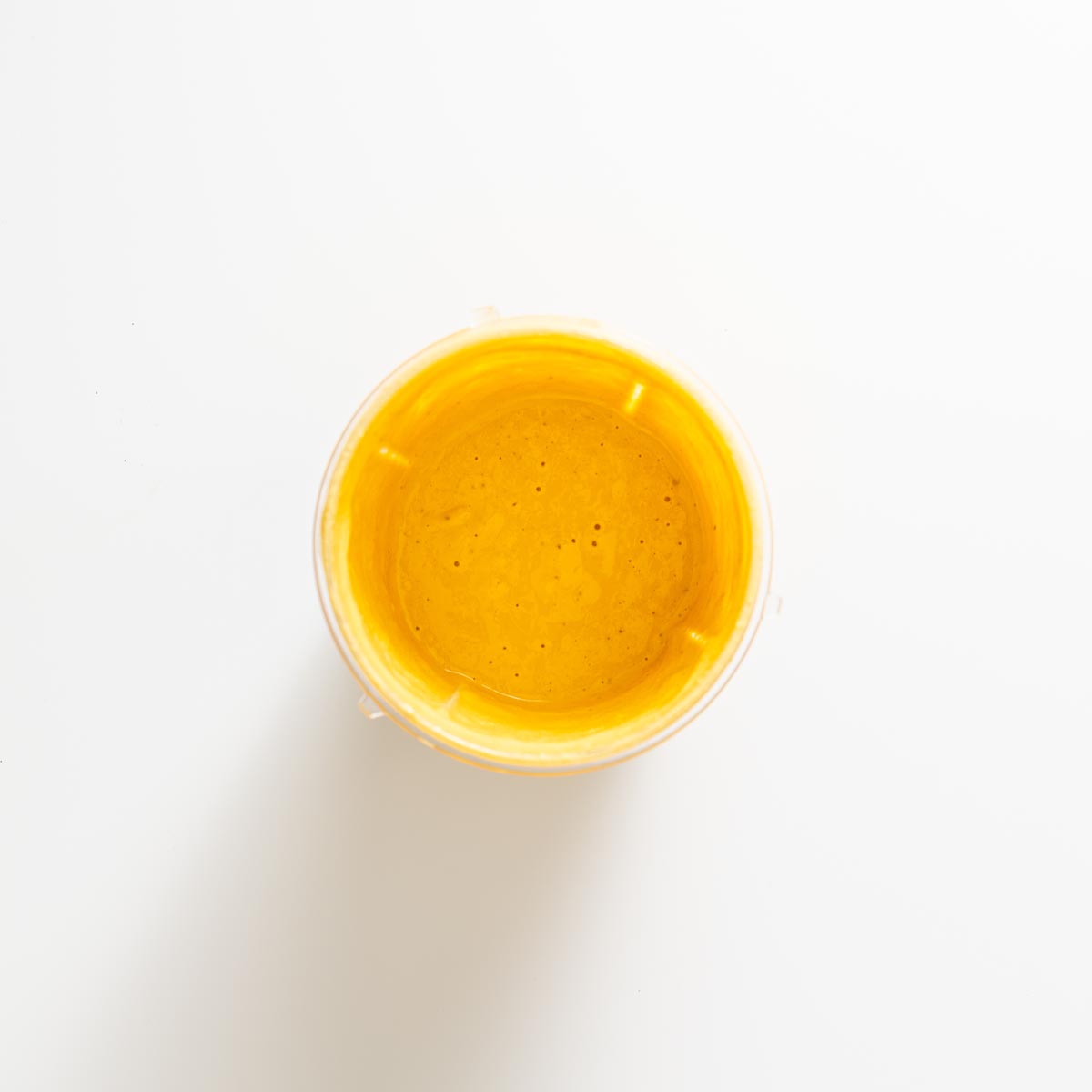 Vibrant miso tahini sauce in a glass bowl on a white surface.