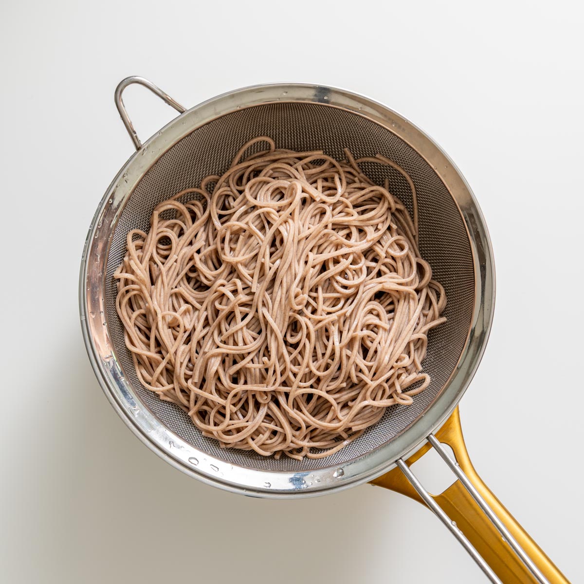 Cooked soba noodles in a metal strainer for miso noodle soup meal prep.