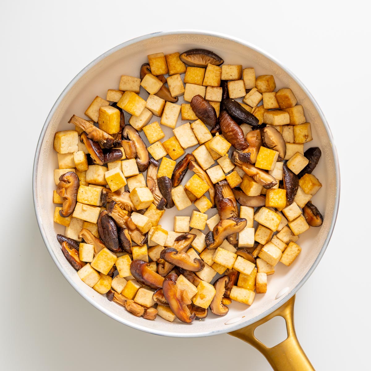 Crispy tofu cubes and sliced shiitake mushrooms cooking in a pan.