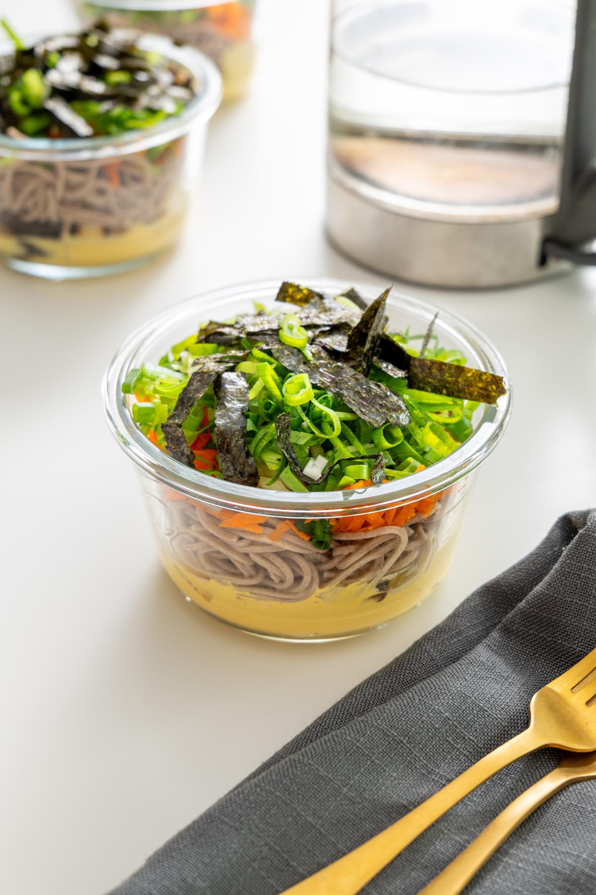 Assembled miso noodle soup meal prep container with toppings on a white surface.