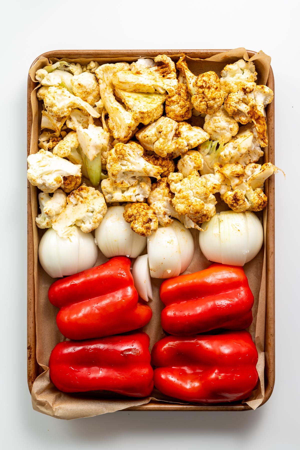 Baking tray with fresh cauliflower florets, onion quarters, and red bell peppers before roasting for soup.