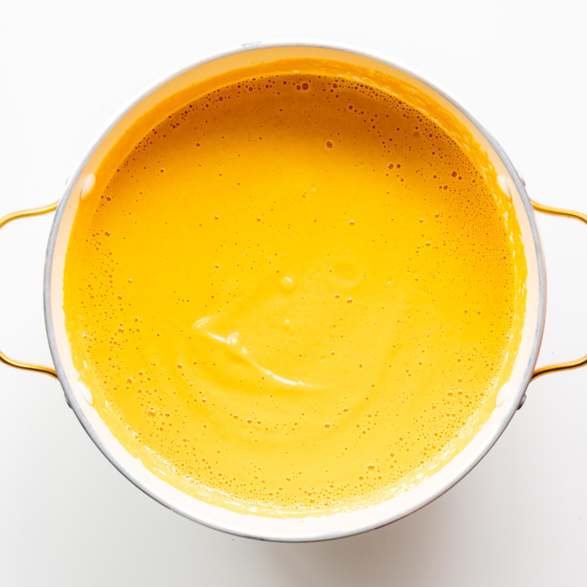 Overhead view of creamy roasted cauliflower and red bell pepper soup in a white pot with gold handles.