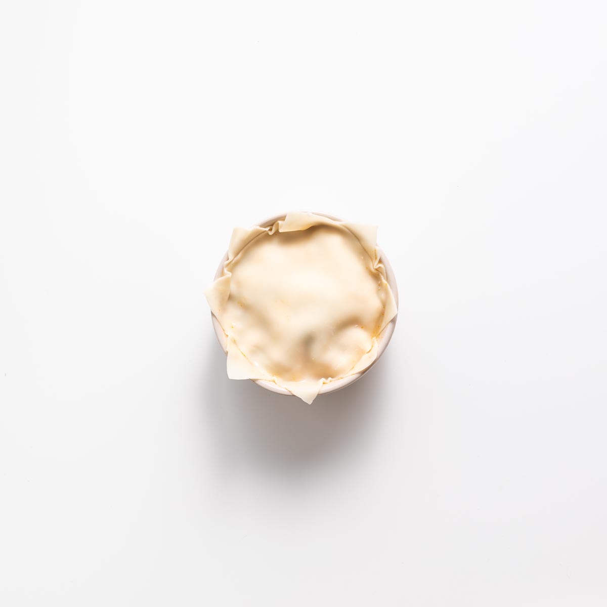 Layering wonton wrapper and filling in a small pink bowl for dumpling soup lasagna