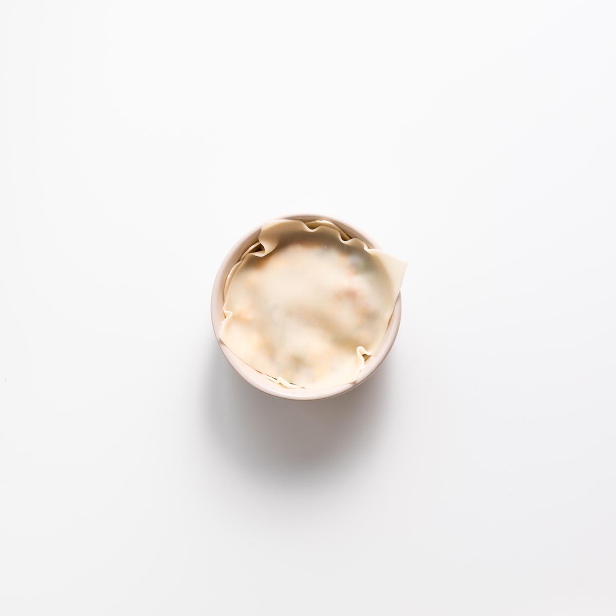 Layering wonton wrapper and filling in a small pink bowl for dumpling soup lasagna