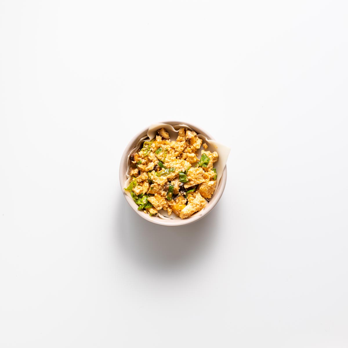 Layering wonton wrapper and filling in a small pink bowl for dumpling soup lasagna