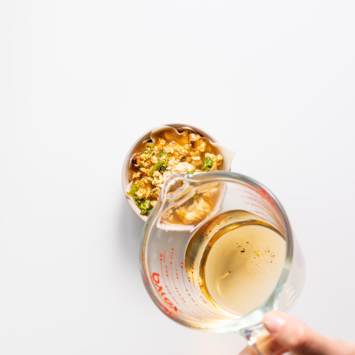 Layering wonton wrapper and filling in a small pink bowl for dumpling soup lasagna