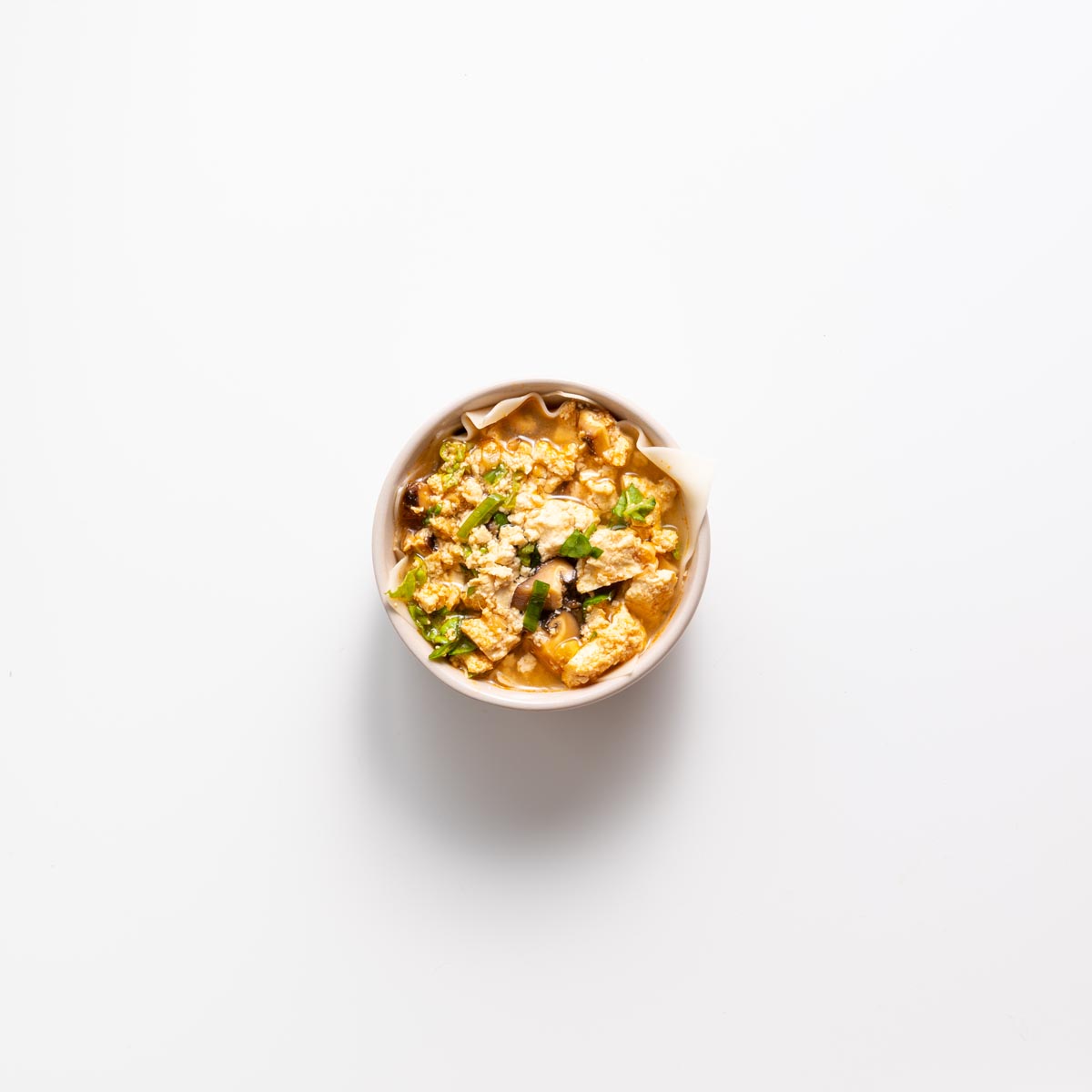 Layering wonton wrapper and filling in a small pink bowl for dumpling soup lasagna