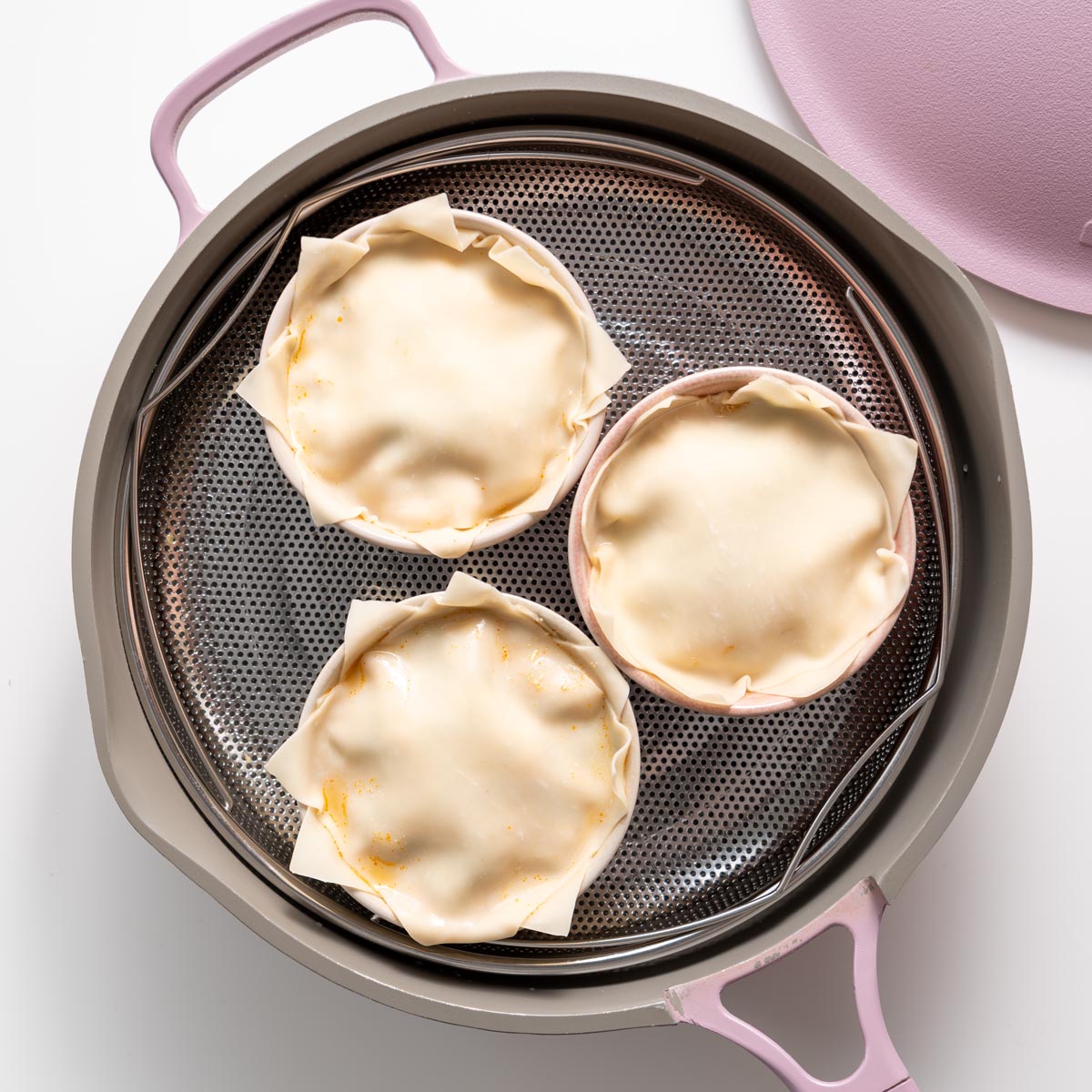 Three bowls of assembled dumpling soup lasagna in a pink steamer basket ready to steam