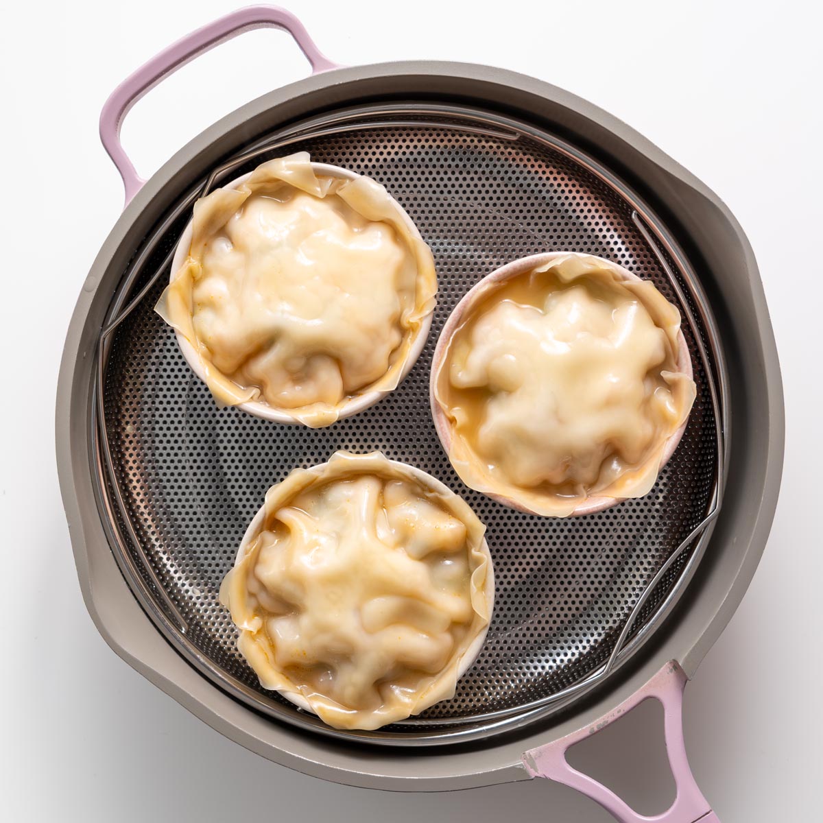 Three bowls of steamed dumpling soup lasagna with puffed wonton wrappers in a pink steamer basket