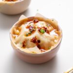Dumpling soup lasagna in a white bowl garnished with chili oil and scallions, with a blurred bowl in the background