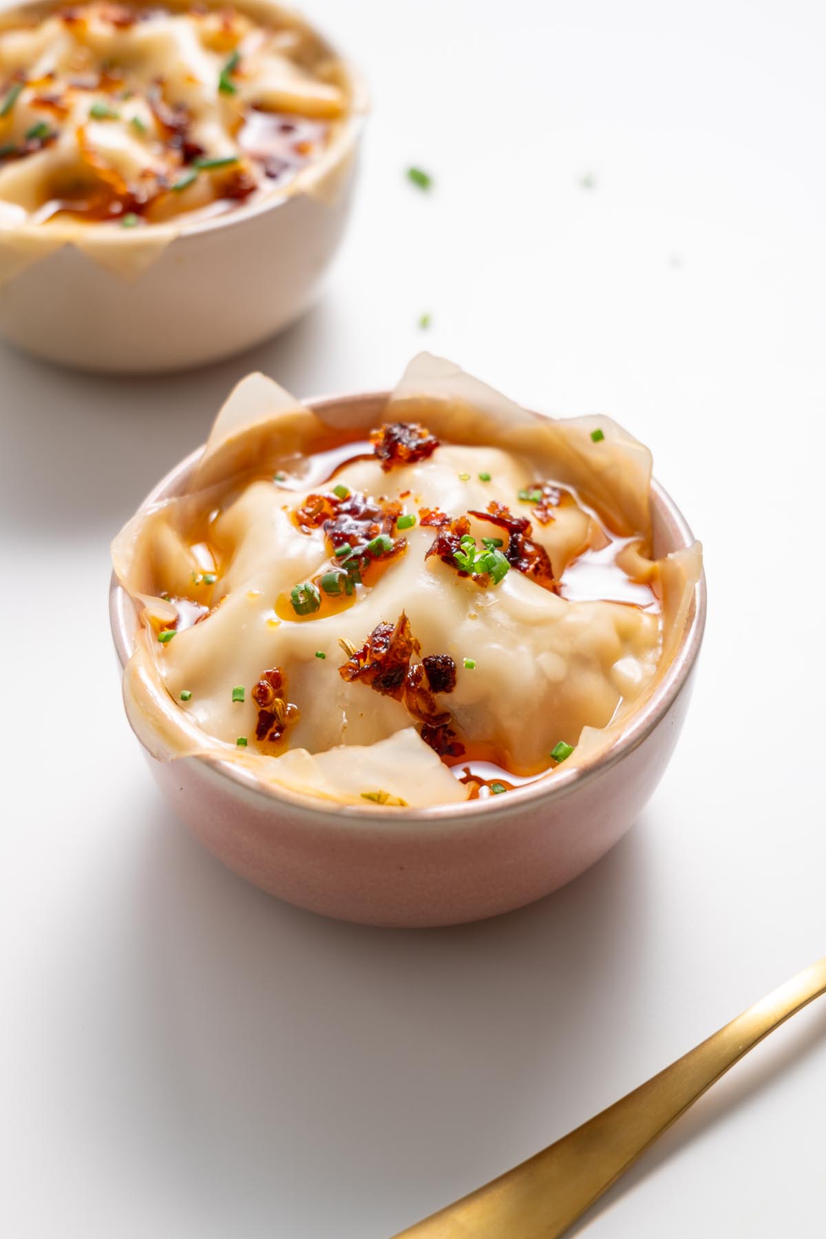 Dumpling soup lasagna in a white bowl garnished with chili oil and scallions, with a blurred bowl in the background