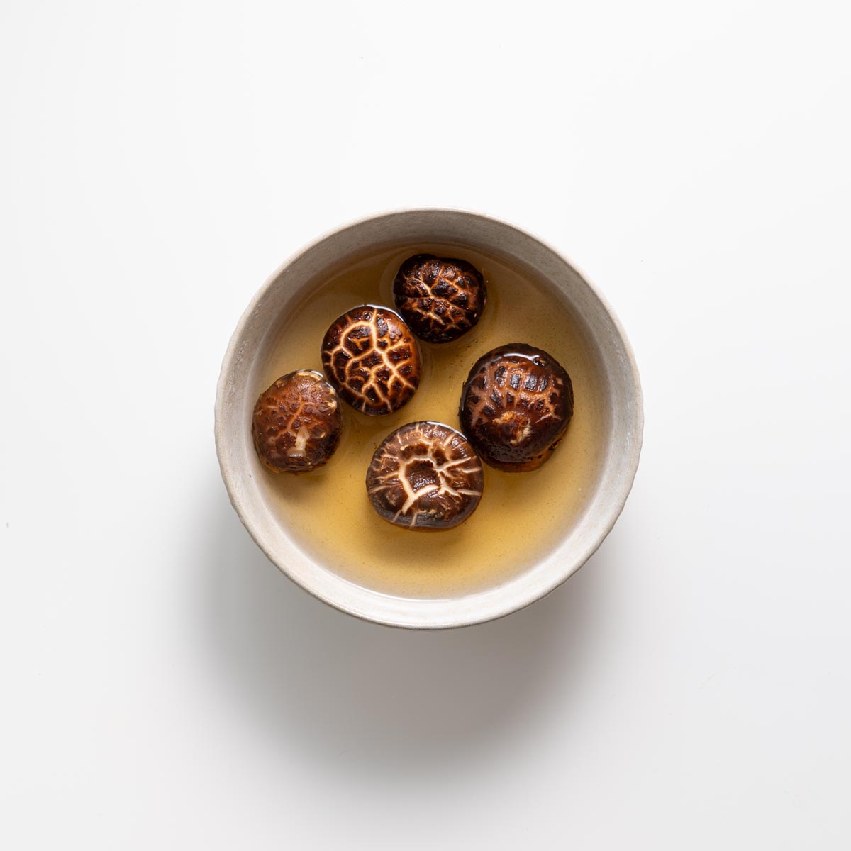 Nấm hương đã bù nước trong nước dùng vàng trong bát kem trên bề mặt trắng