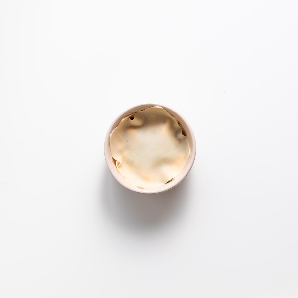 Layering wonton wrapper and filling in a small pink bowl for dumpling soup lasagna