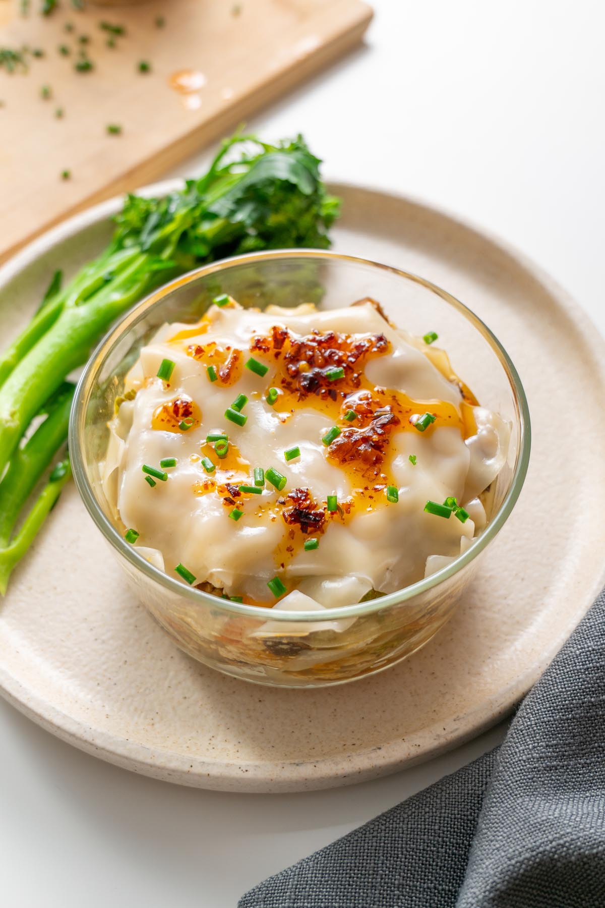 Steamed soup dumpling lasagna in a glass bowl topped with chili oil and scallions.