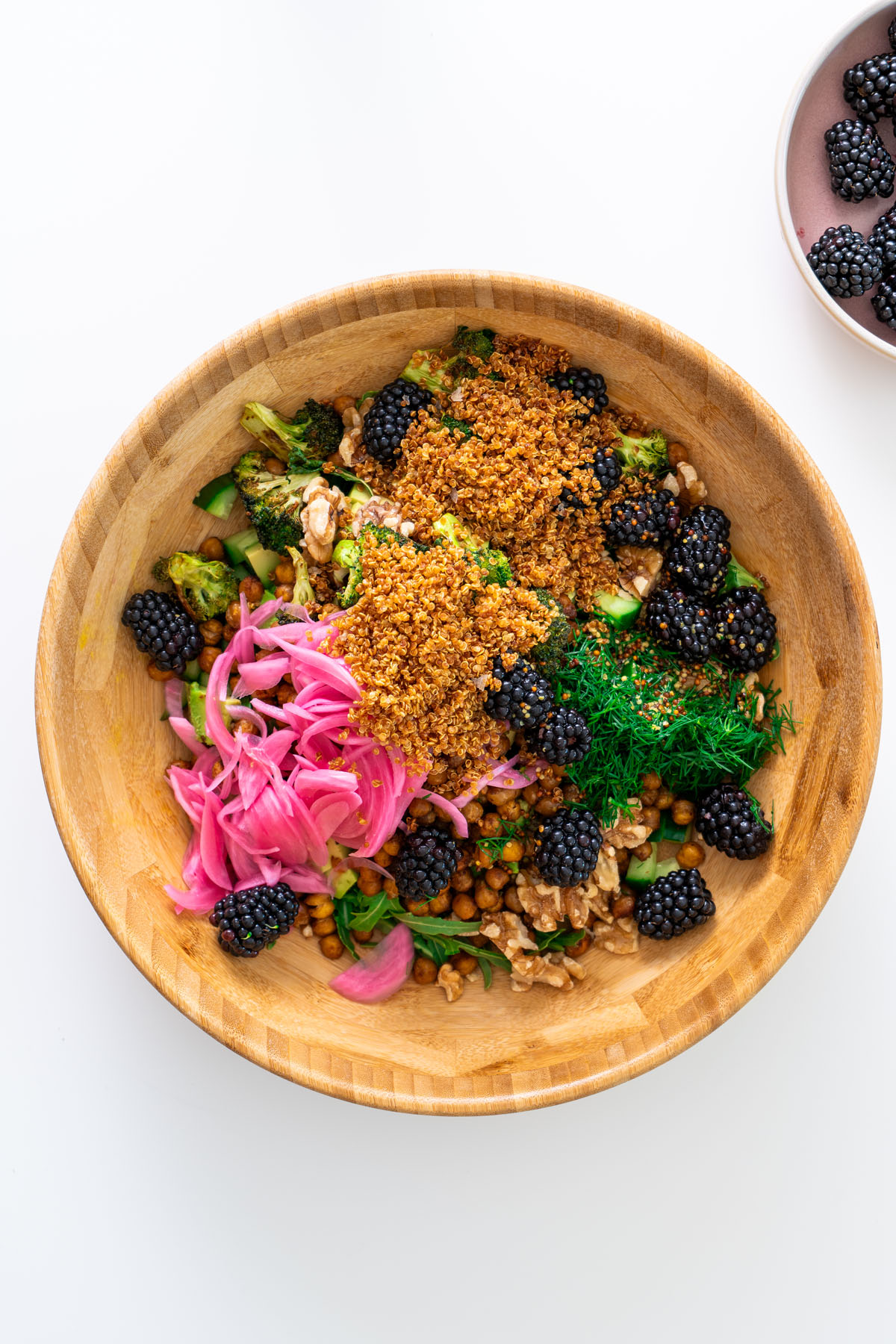 Overhead view of crispy quinoa and blackberry salad with pickled onions, dill, walnuts, chickpeas, and roasted broccoli in a wooden bowl.