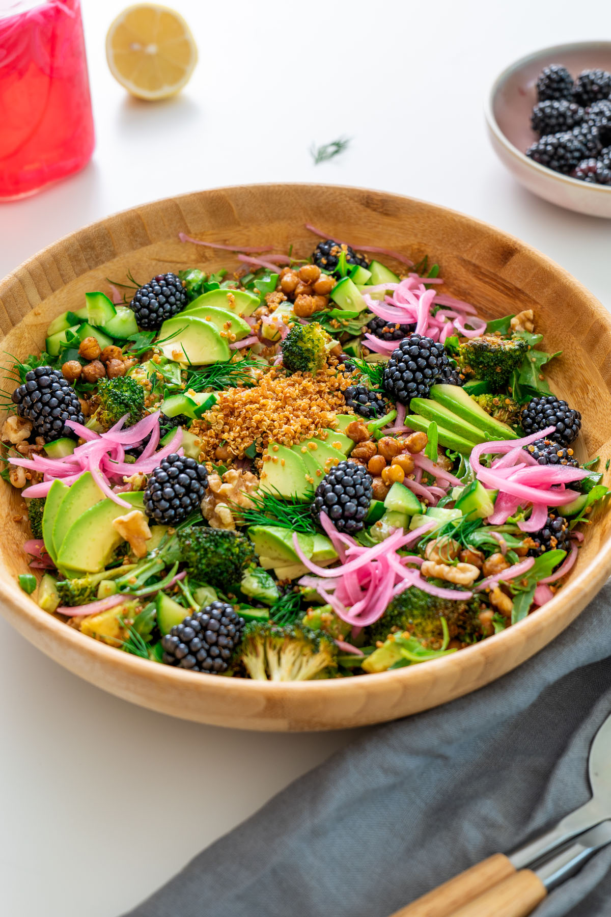 Crispy quinoa and blackberry salad in a wooden bowl on a table with extra blackberries and pickled onions nearby.