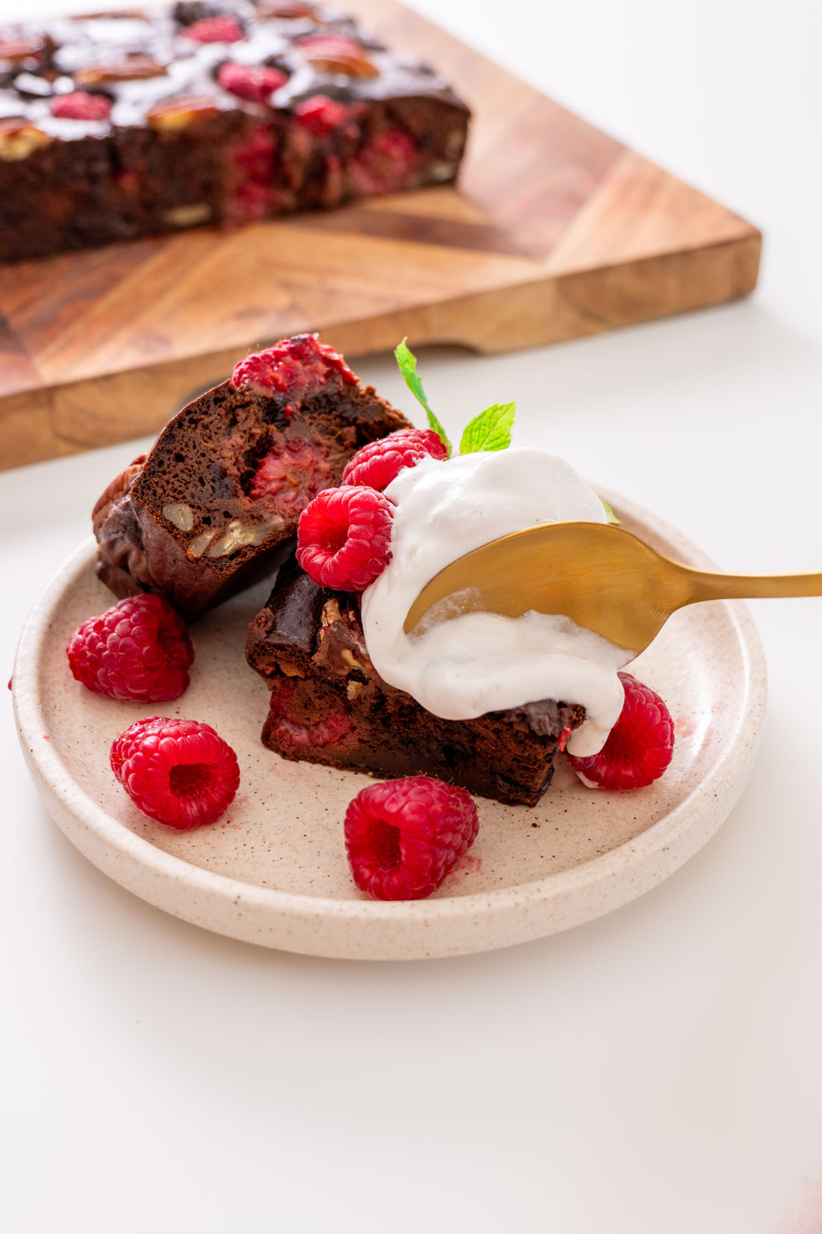 A fudgy sweet potato brownie topped with vanilla ice cream and fresh raspberries on a ceramic plate.