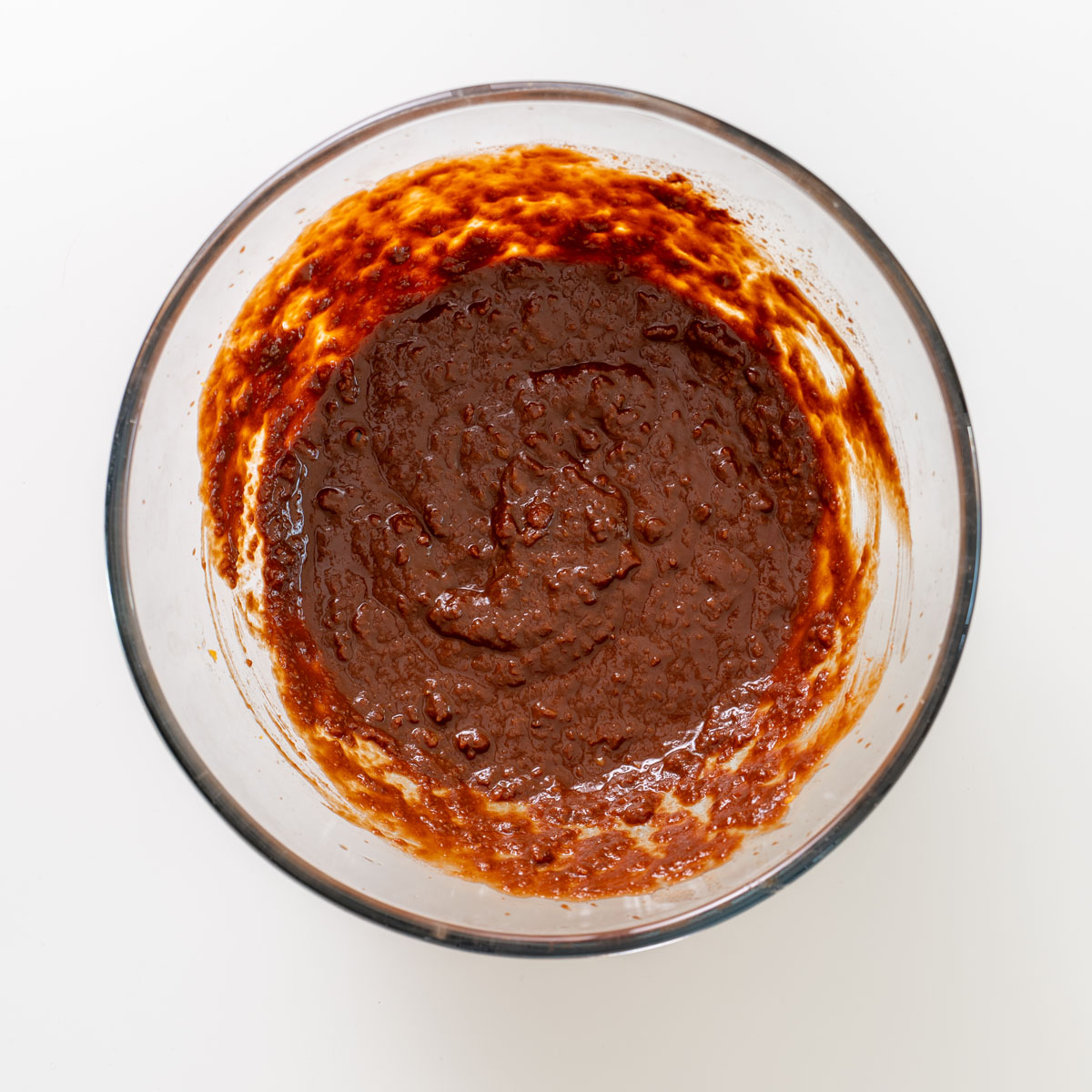 Thick chocolate brownie batter in a glass mixing bowl before smoothing into the pan.