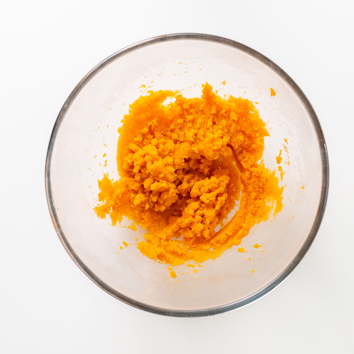 Mashed cooked sweet potato in a glass mixing bowl.