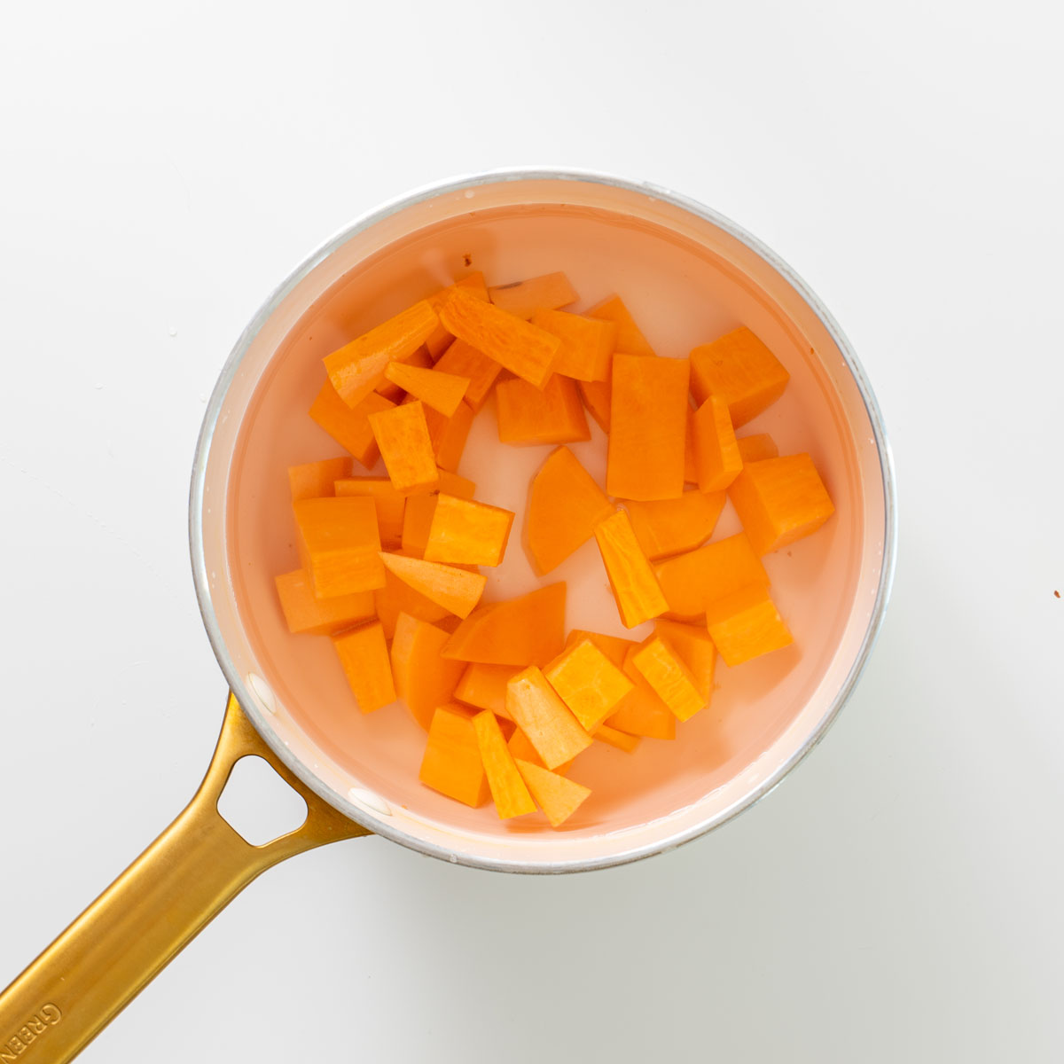 Chopped sweet potato cubes in a saucepan filled with water before cooking.